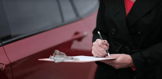 ustomer signing car delivery documents on a clipboard with vehicle in background