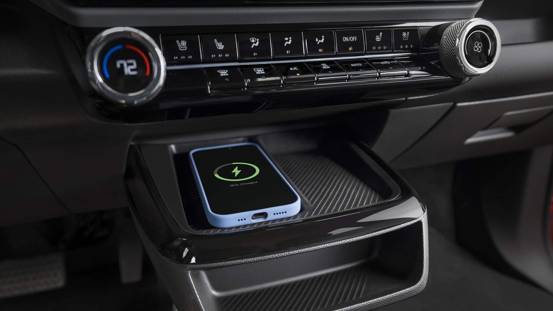 Smartphone wirelessly charging in car, placed in a dashboard slot near climate controls displaying 72°F.