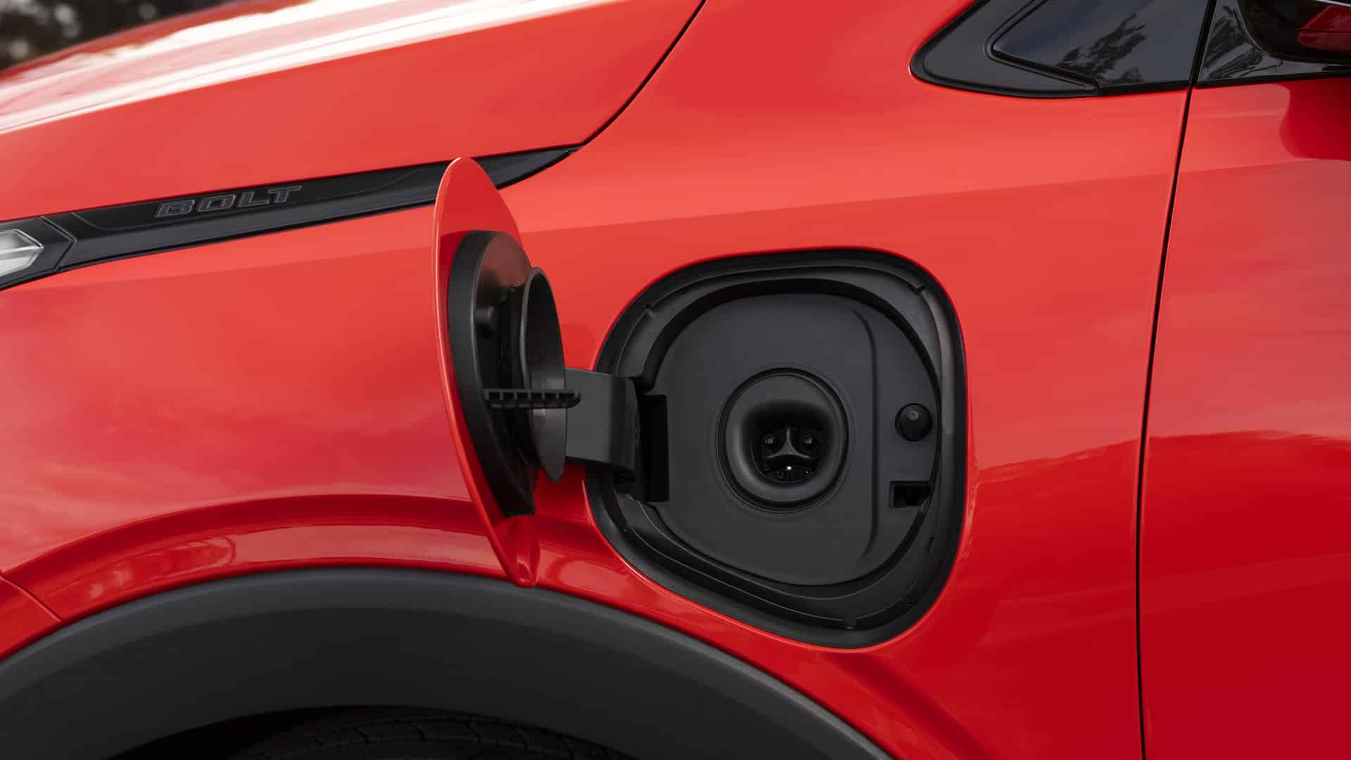 Red electric car with open charging port and "Bolt" emblem.