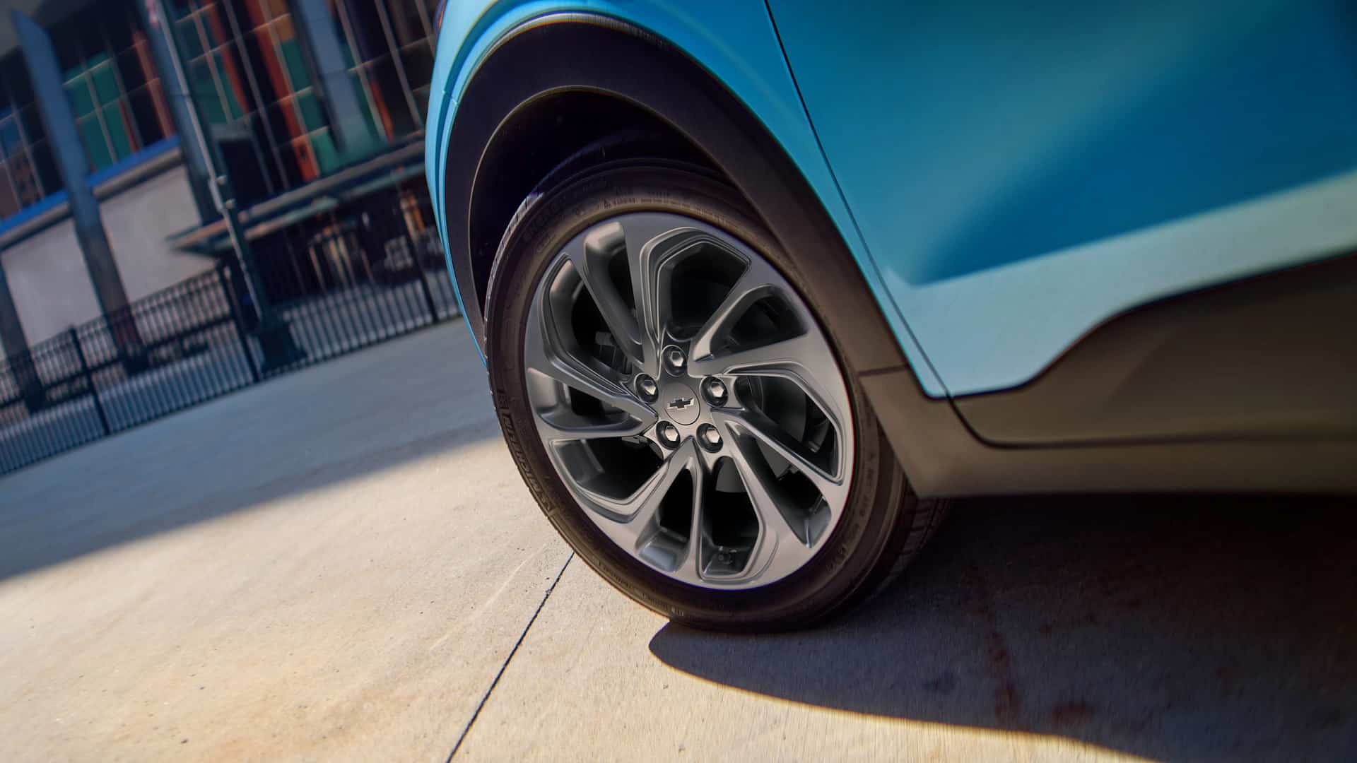 Close-up of a car tire and wheel on a blue vehicle, parked on a concrete surface.