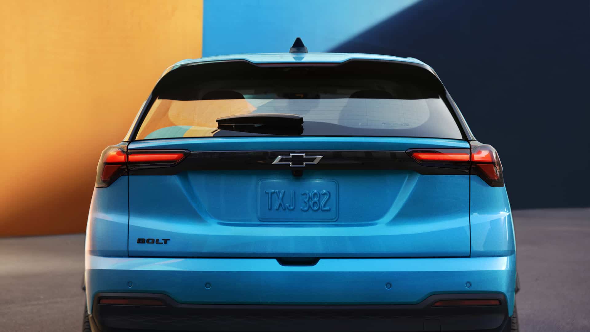 Rear view of a blue Chevrolet Bolt EV against a vibrant orange and blue background.