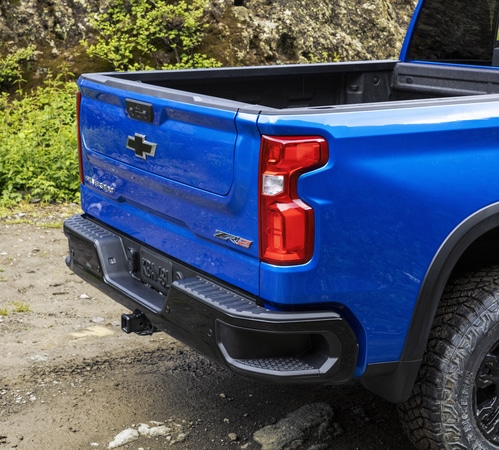 Rear view of a blue Chevrolet pickup truck on a gravel road, with earthy background.