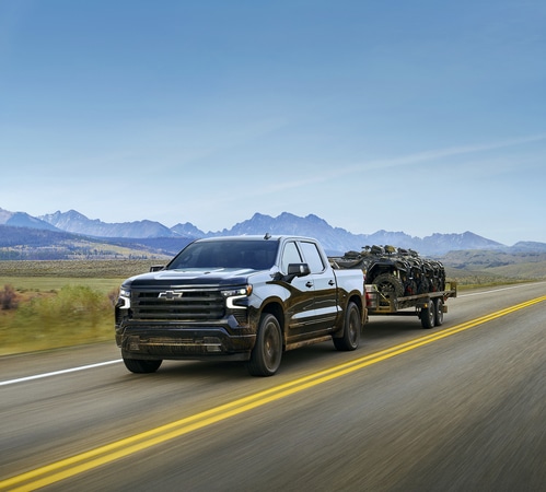 Chevrolet Silverado towing a trailer on a highway with mountain scenery.