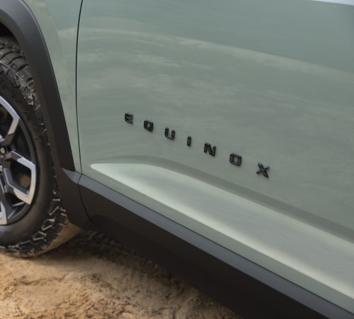 Close-up of a light green car door with "EQUINOX" logo and rugged tire on sandy terrain.
