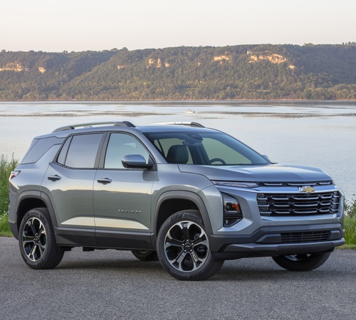 Silver SUV parked by a lake with hills in the background under a clear sky.