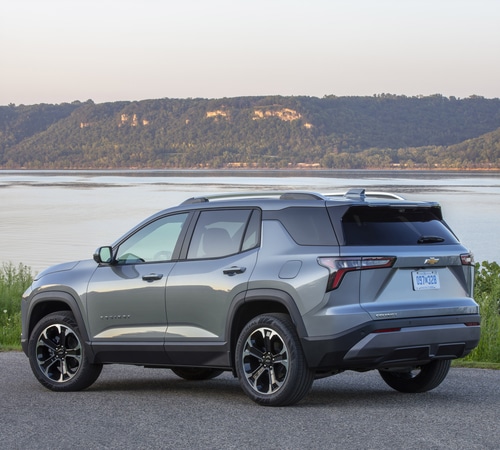 A gray SUV parked by a scenic lake with hills in the background on a clear day.