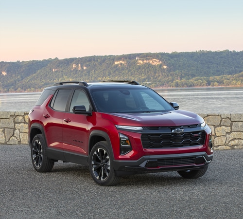 Red SUV parked by a stone wall with a lake and hills in the background at sunset.