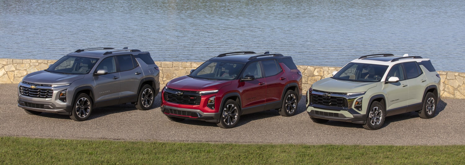A shiny red SUV is parked in a dimly lit urban setting at night. The car features a sleek design with distinctive wheel rims, and illuminated headlights, reflecting light on the wet pavement. Modern architectural elements are visible in the background.