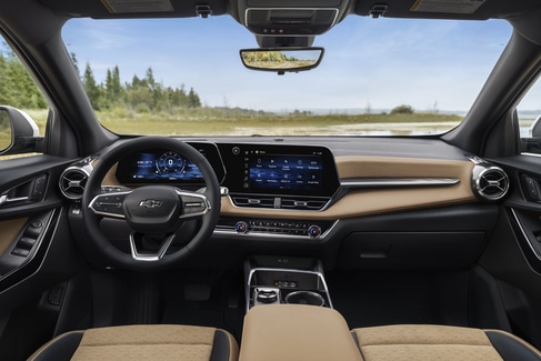 View from the backseat of a car showing two people in the front seats. The driver is holding the steering wheel. The sunroof is open, revealing a blue sky and tall buildings outside. The dashboard and rearview mirror are visible.