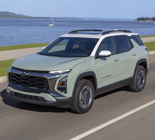 Green SUV driving along a coastal road with water and blue sky in the background.