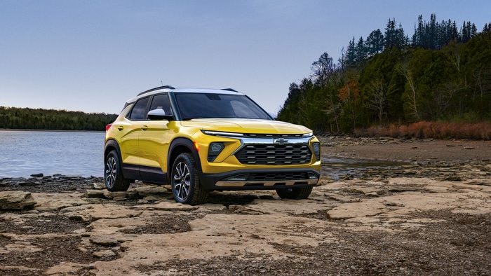 Yellow SUV parked on rocky terrain by a lake with forested background.
