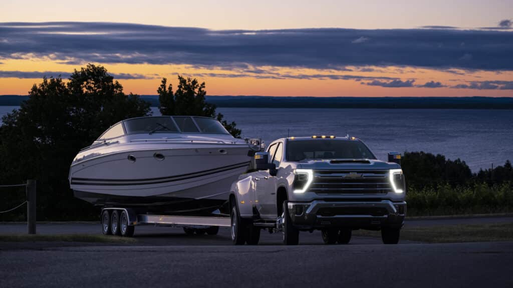White truck towing a boat at sunset by a lake, highlighting adventure and exploration.