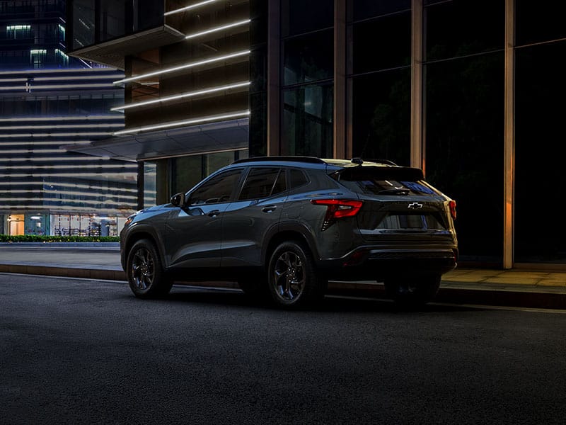 SUV parked on a city street at night, with modern building lights in the background.