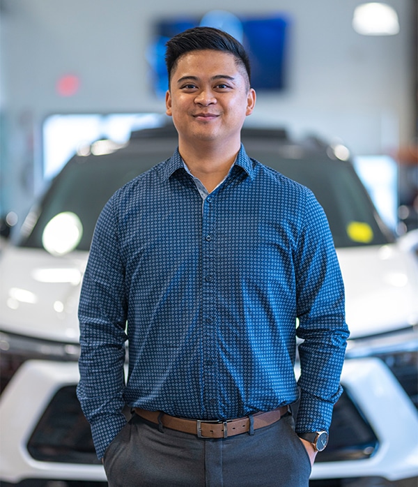 Man in a blue shirt standing confidently in front of a white car in a showroom.