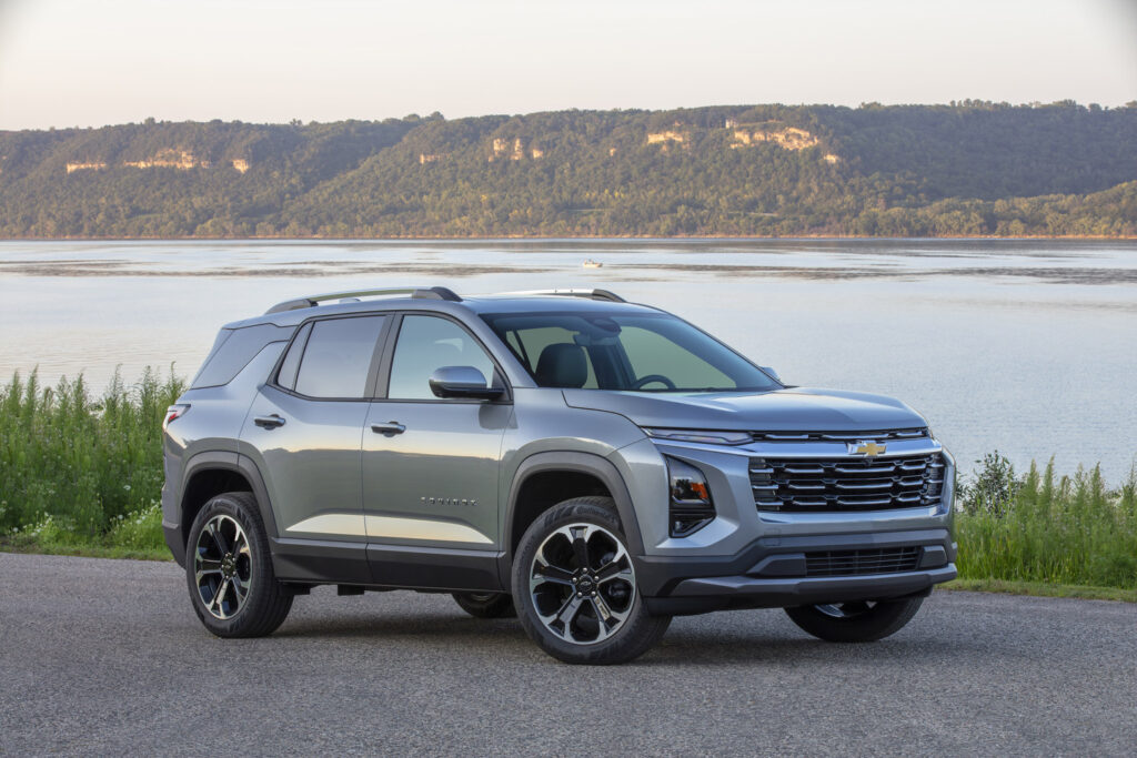 Silver SUV parked by a scenic lake with forested hills in the background.