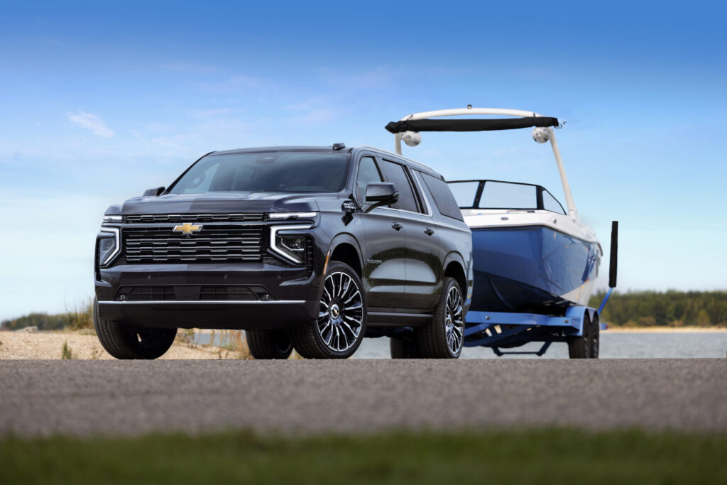 SUV towing a blue boat on a trailer against a clear blue sky, parked near a water body.