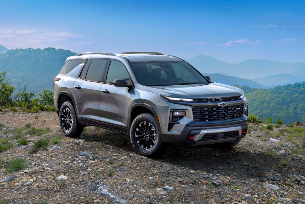 Silver SUV on rocky terrain with lush green hills in the background under a clear blue sky.