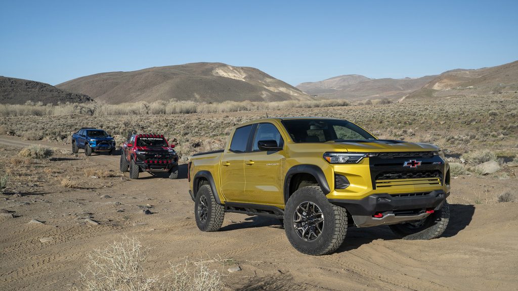 Three Chevrolet trucks, including a yellow model, drive off-road through a desert landscape.