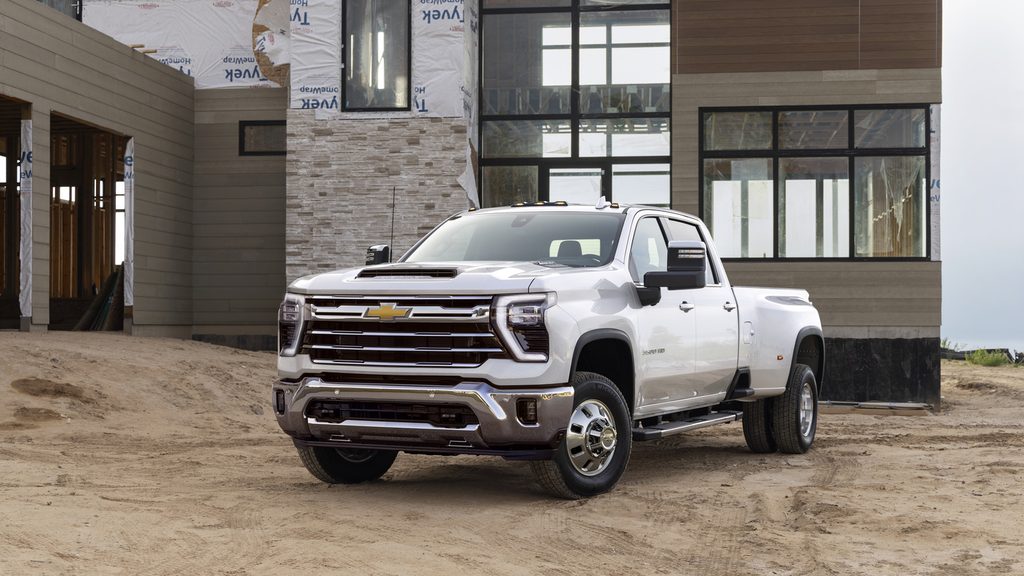 White Chevrolet truck parked on sandy terrain in front of a modern building under construction.