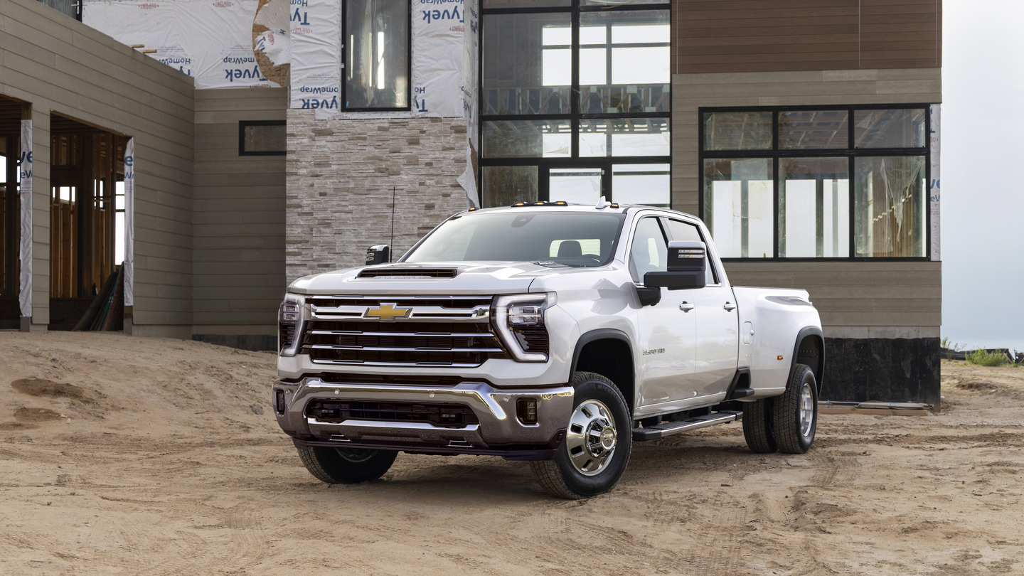 White Chevrolet truck parked on sandy terrain in front of a modern building under construction.