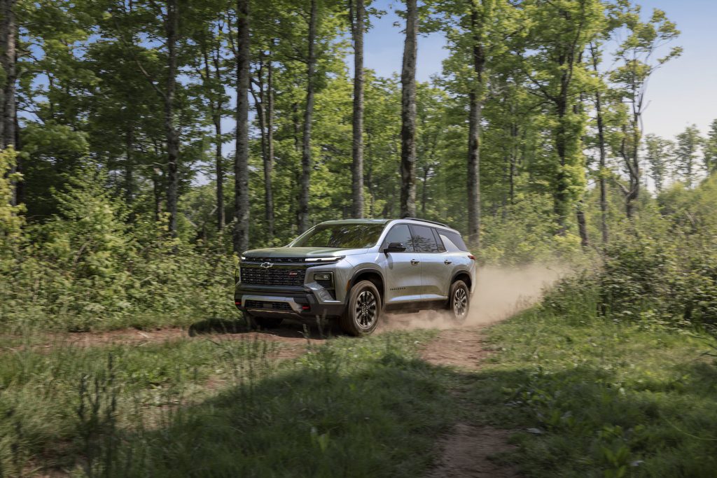 A silver SUV driving through a lush forest trail, kicking up dust on a sunny day.