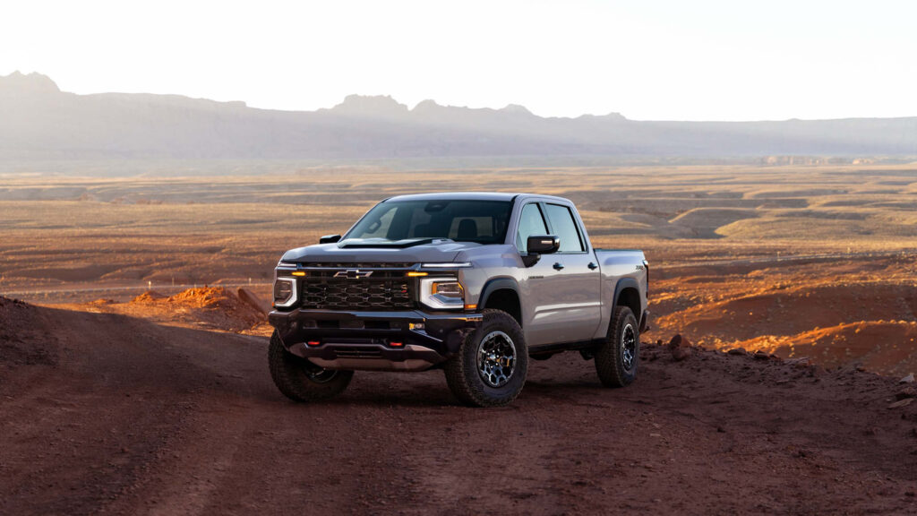 Silver pickup truck on a rugged dirt road with a vast desert landscape under a clear sky.